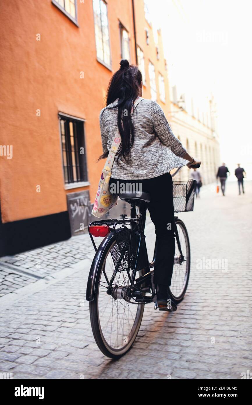 Rear view of woman standing with bicycle on cobbled street Stock Photo