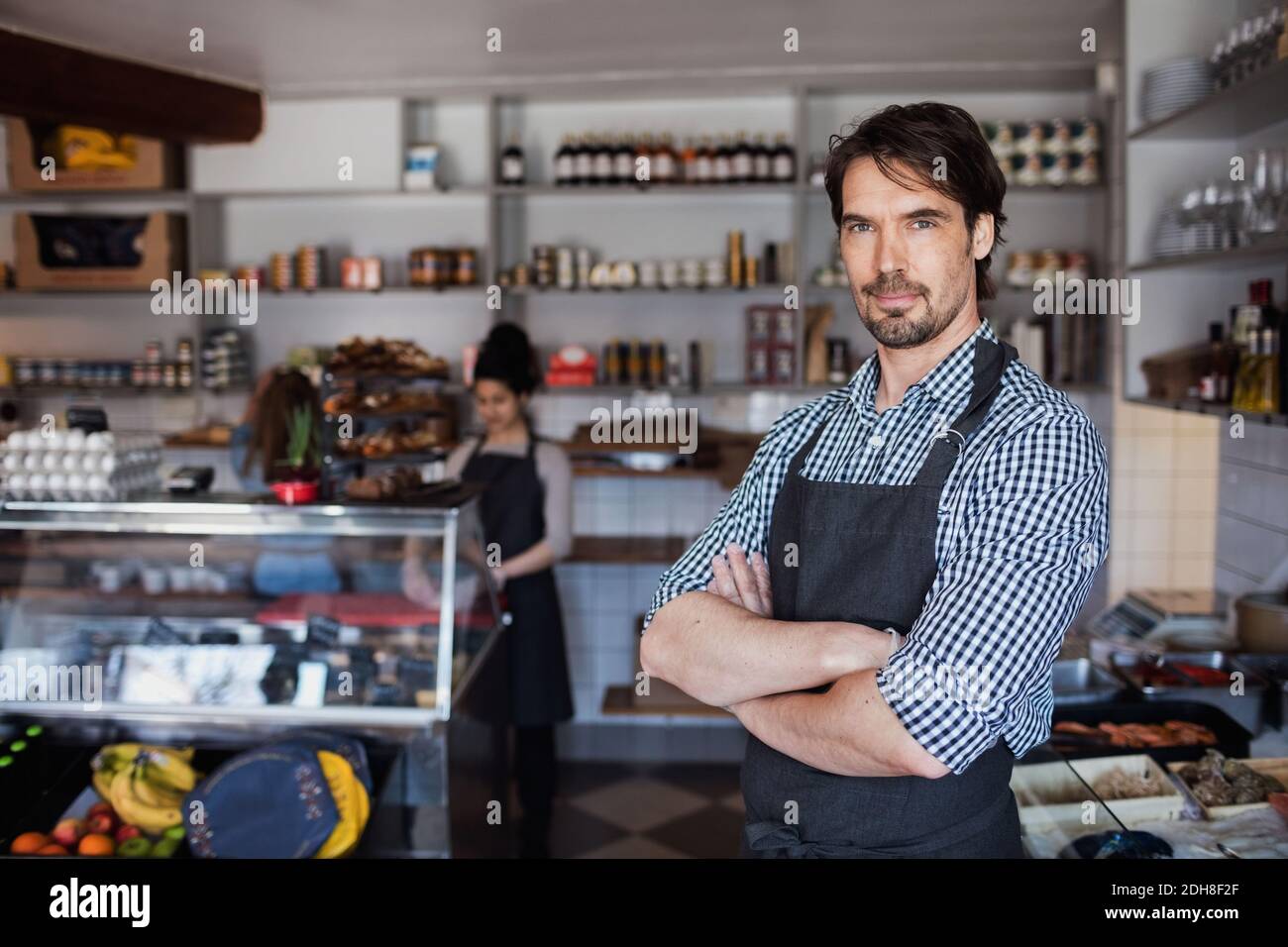 Portrait of confident owner standing with arms crossed against colleague in store Stock Photo