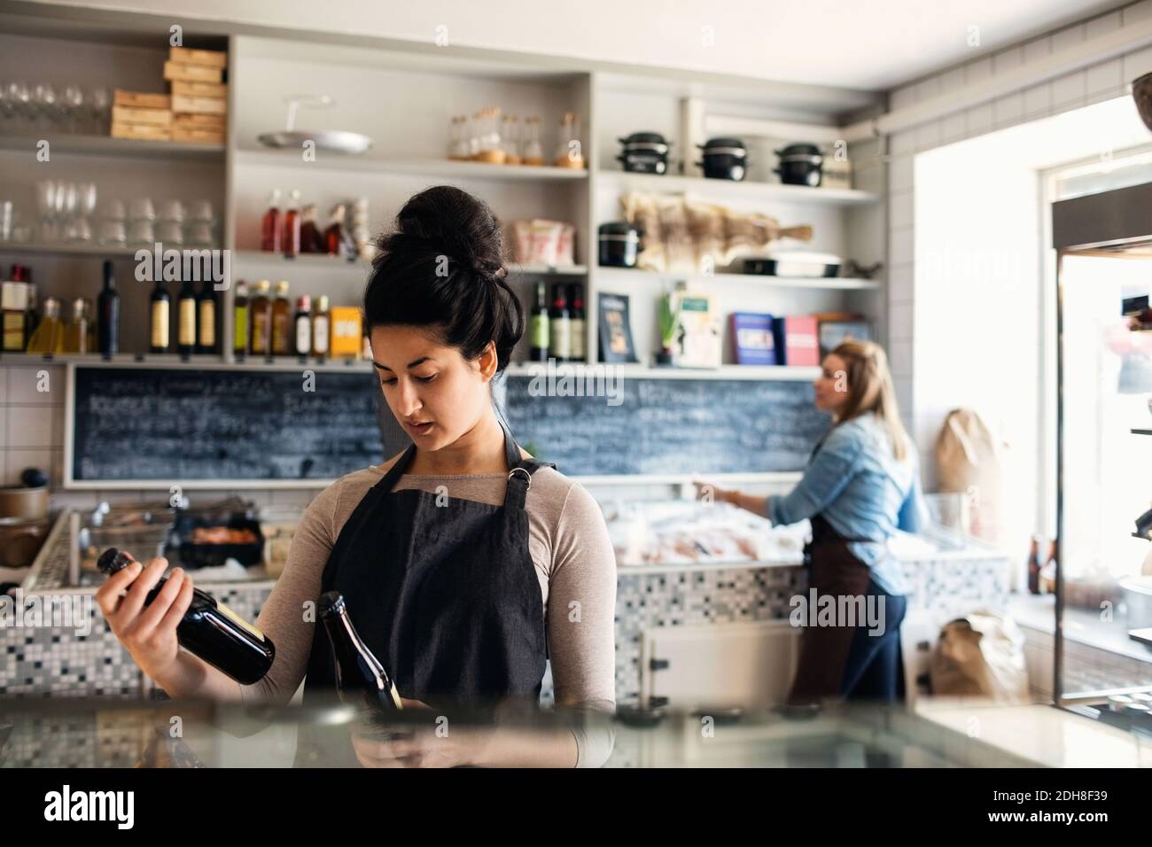 Confident woman checking bottles while colleague standing in background at retail display Stock Photo