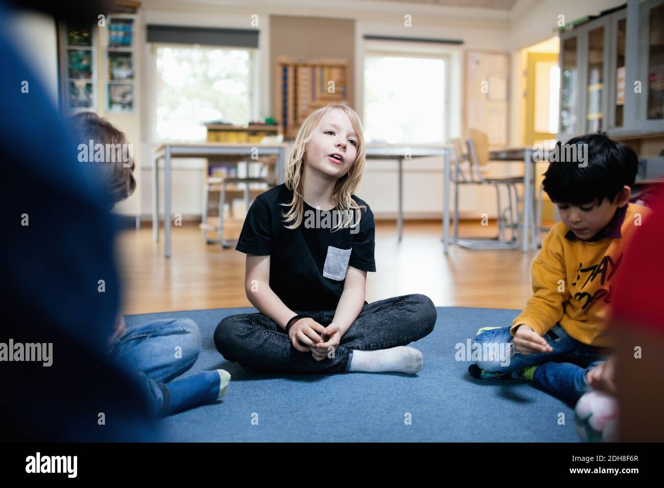 Girl talking while sitting with friends on floor in classroom Stock Photo