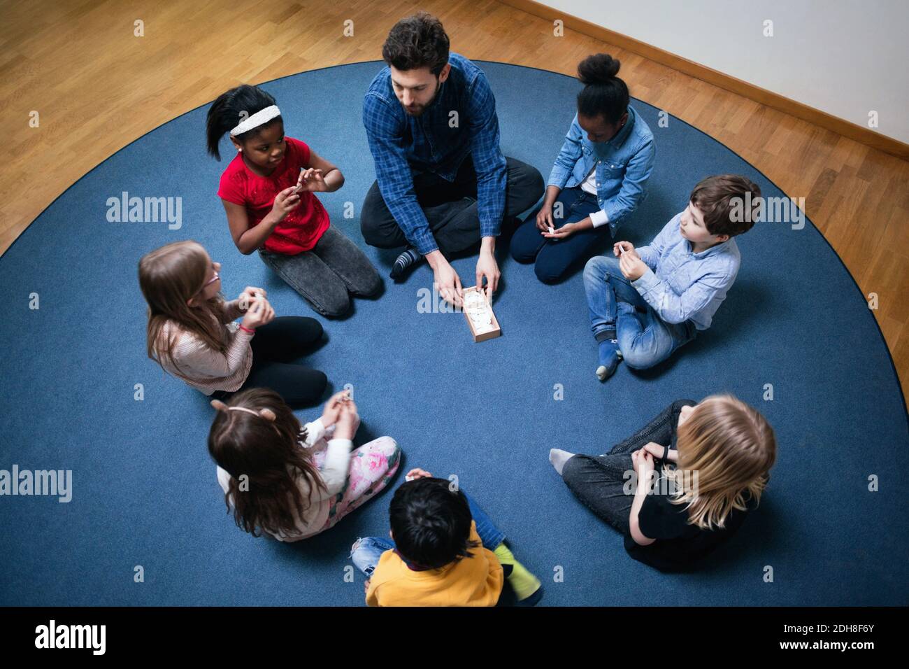 High angle view of teacher playing with children on floor at school Stock Photo