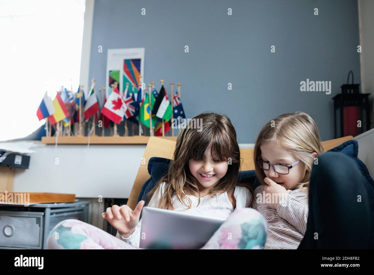 Smiling friends using digital tablet while sitting on sofa in school Stock Photo