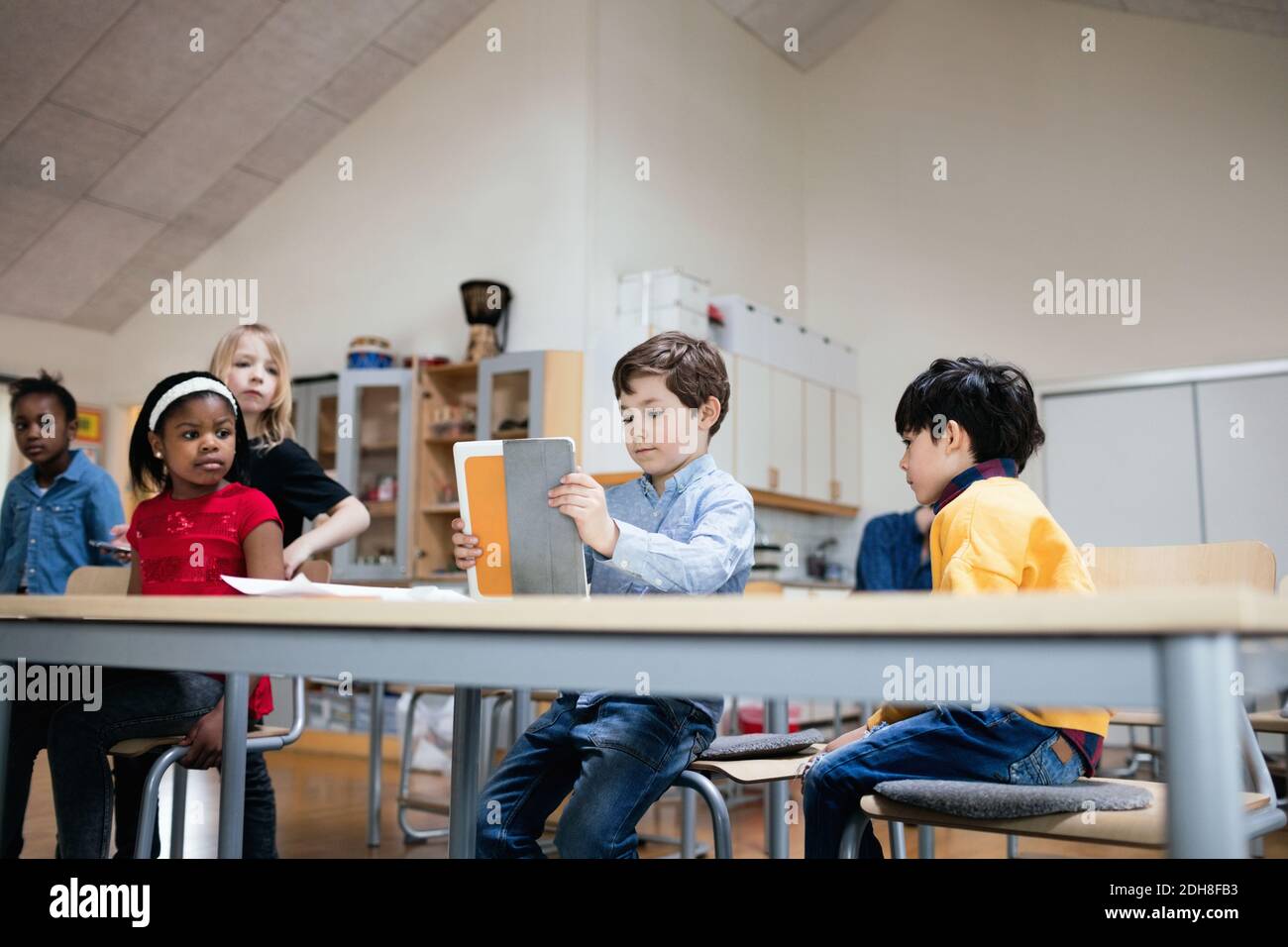 Students looking at boy using digital tablet in classroom at school Stock Photo