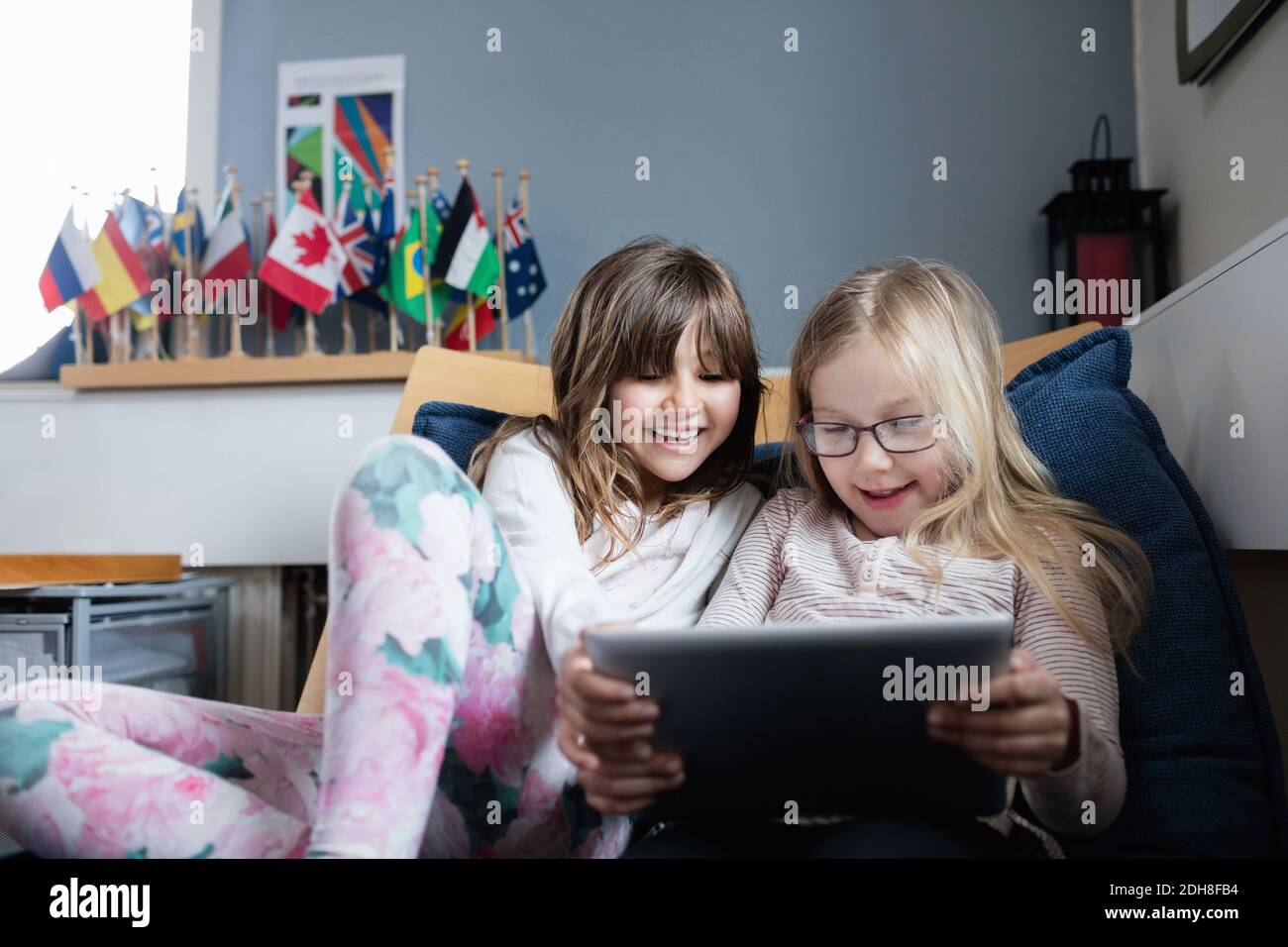 Smiling friends using digital tablet while resting on sofa in school Stock Photo