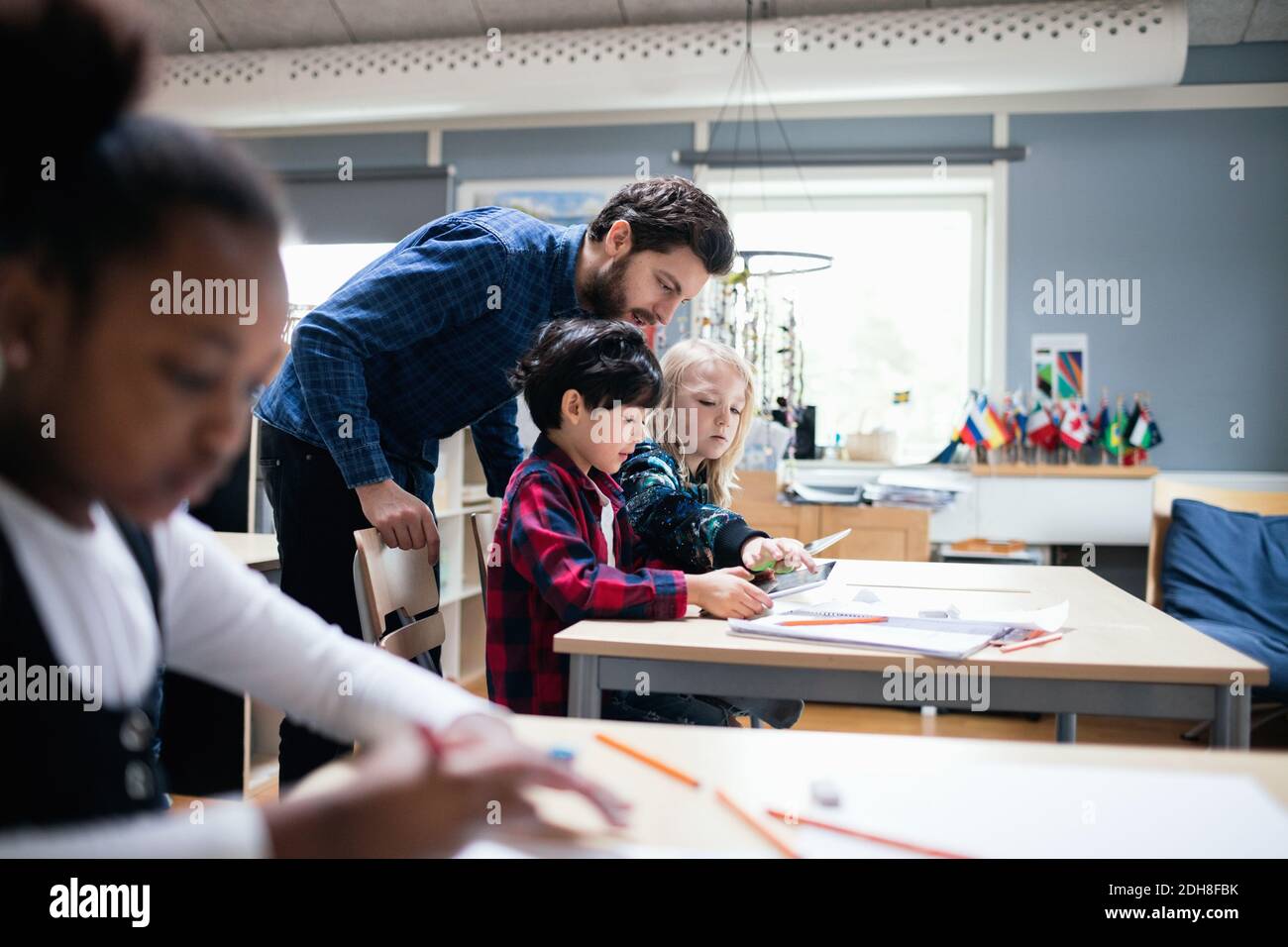 Teacher looking at boy and girl using digital tablet in classroom Stock Photo