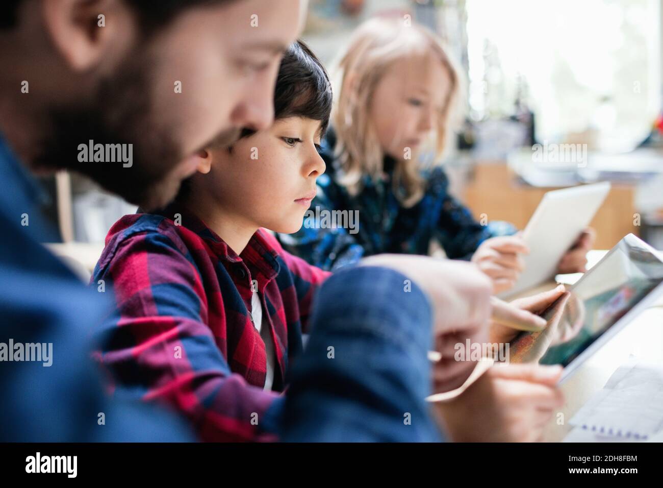 Close-up of teacher explaining students to use digital tablet at desk Stock Photo