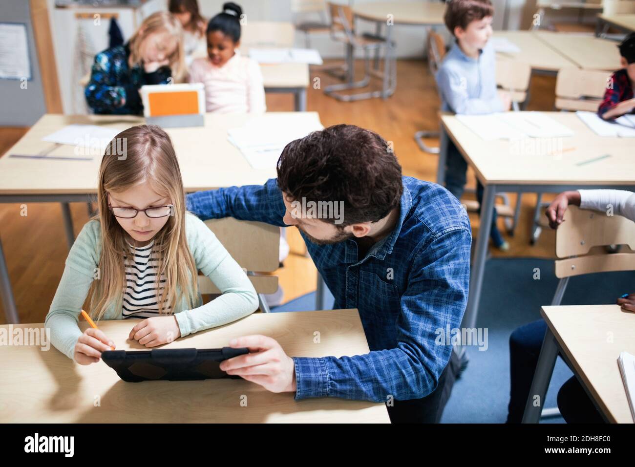 High angle view of teacher assisting female student while using digital tablet in classroom Stock Photo