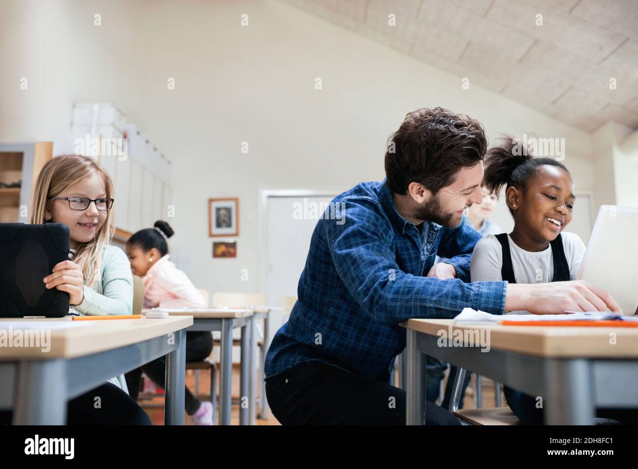Smiling teacher with students using digital tablet at classroom Stock Photo