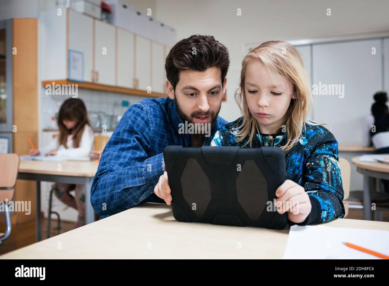Male teacher explaining student in using digital tablet at classroom Stock Photo
