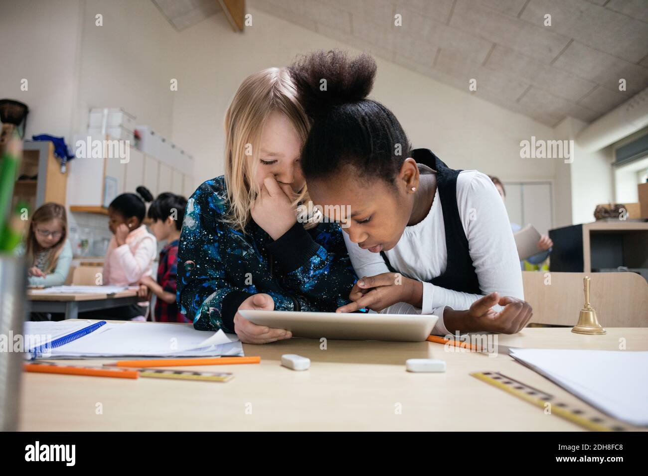 Multi-ethnic students using digital tablet at desk in classroom Stock Photo