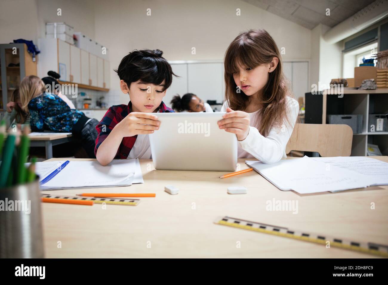 Concentrated students using digital tablet at desk in classroom Stock Photo