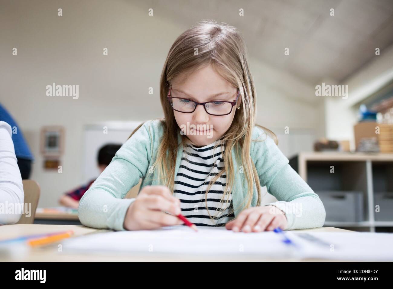 Concentrated girl wearing eyeglasses writing at classroom desk in school Stock Photo