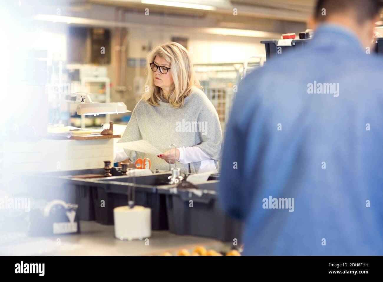 Woman reading paper while volunteer standing by production line at workshop Stock Photo
