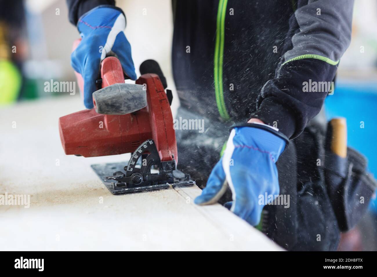 Midsection of manual worker using jigsaw on wooden planks at site Stock Photo