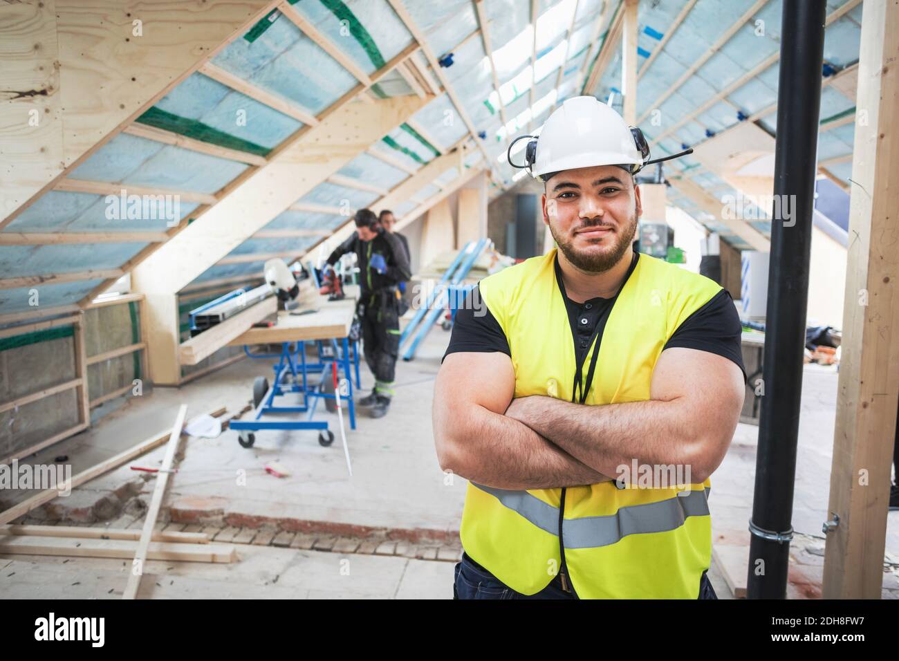 Portrait of confident manual worker standing with arms crossed at construction site Stock Photo