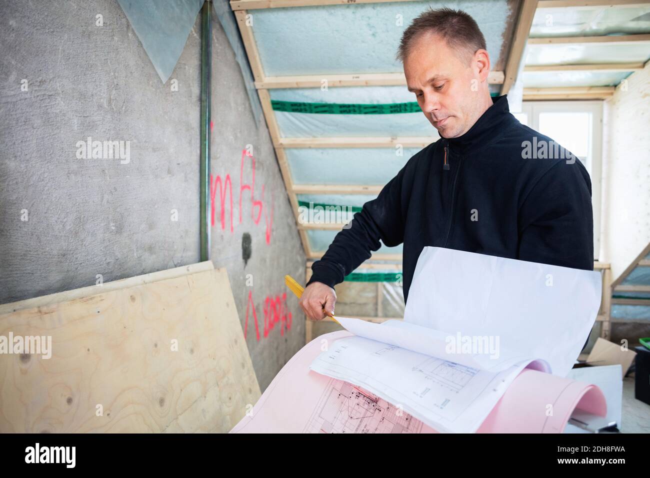 Serious manual worker reading blue prints while standing at construction site Stock Photo