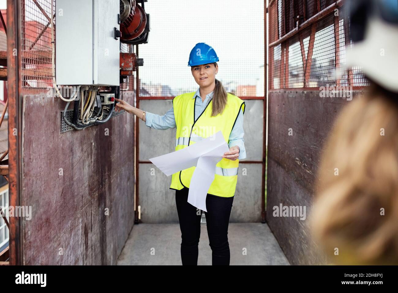 Construction manager holding documents while showing machinery in construction elevator Stock Photo