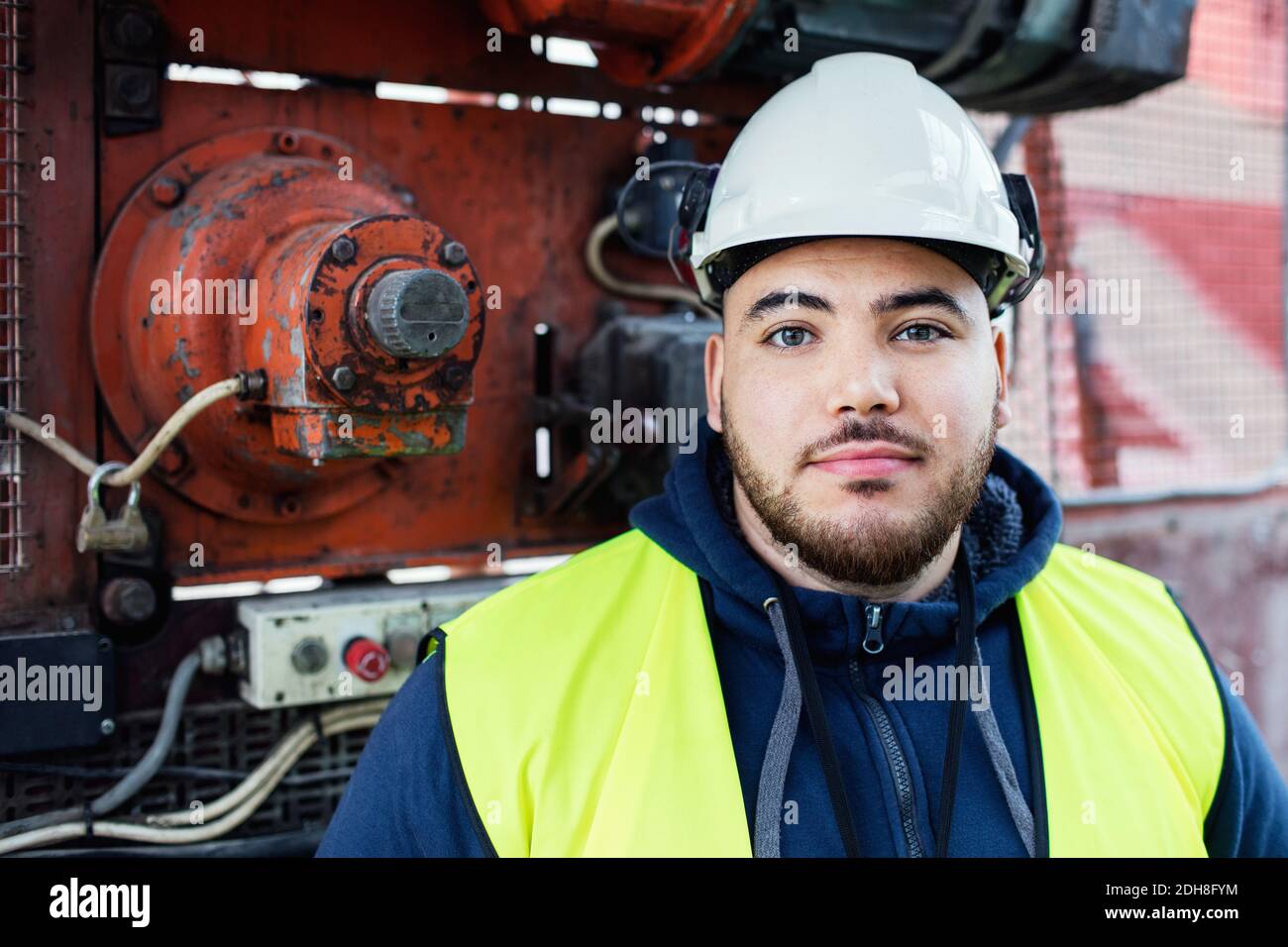 Portrait of confident manual worker standing against machinery in industry Stock Photo