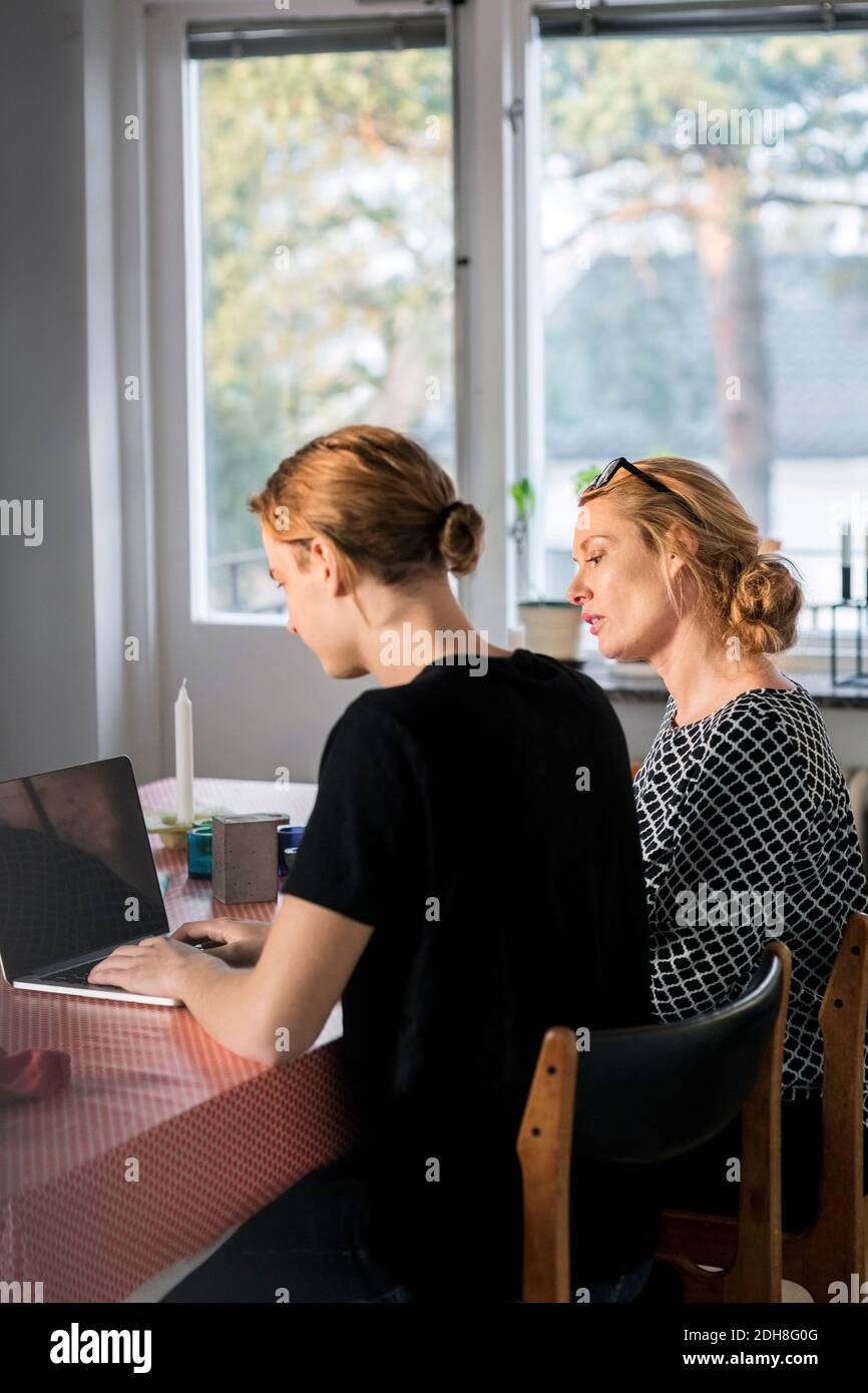 Mother and son using laptop at dining table by window Stock Photo