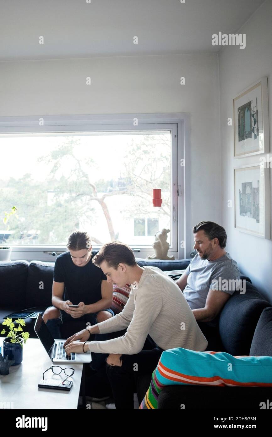 Men using technologies while sitting with father in living room Stock Photo