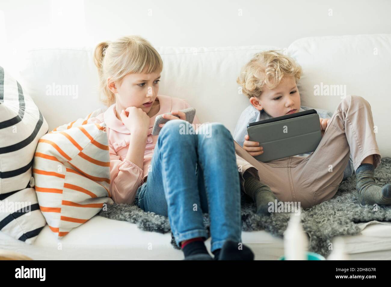 Siblings using digital tablet and mobile phone at home Stock Photo