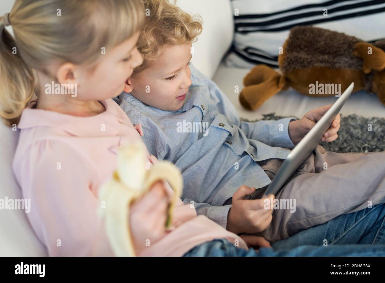 Siblings using digital tablet while eating banana at home Stock Photo