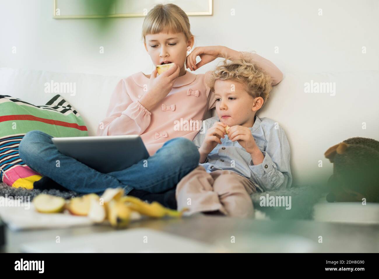 Siblings using digital tablet while eating apples at home Stock Photo