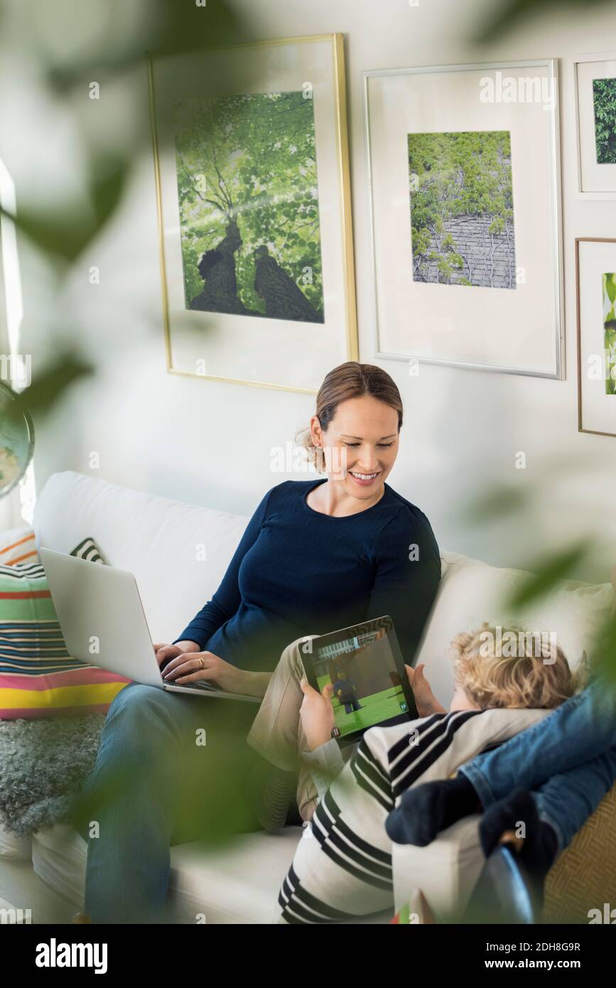 Happy mother looking at boy using digital tablet Stock Photo