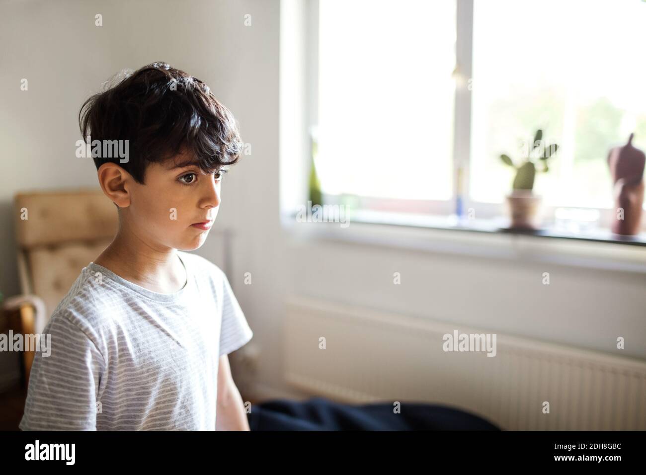 Thoughtful boy standing by window at home Stock Photo