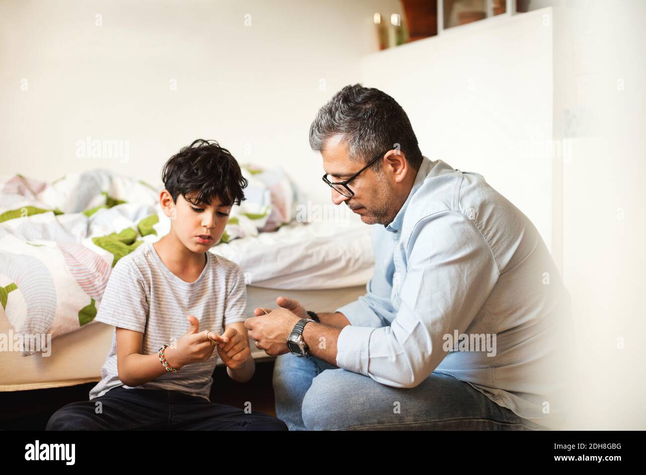 Father and son playing with rubber bands by bed at home Stock Photo