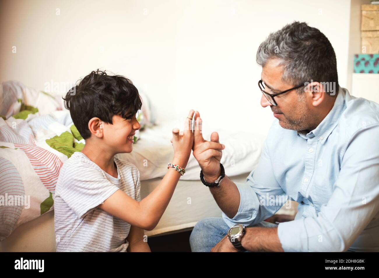 Smiling father and son playing with rubber bands while sitting at home Stock Photo