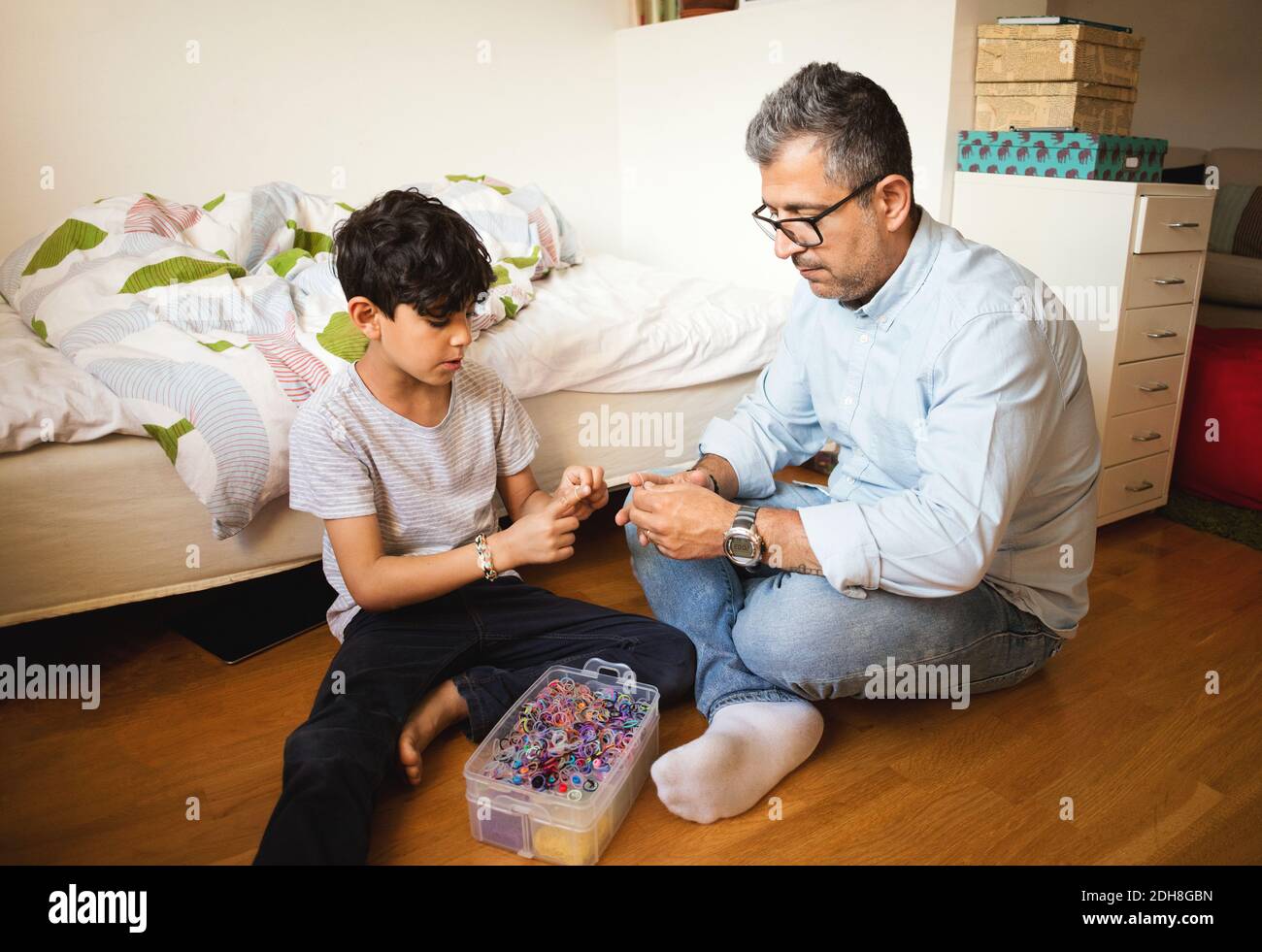 Father and son playing with rubber bands while sitting on hardwood floor at home Stock Photo