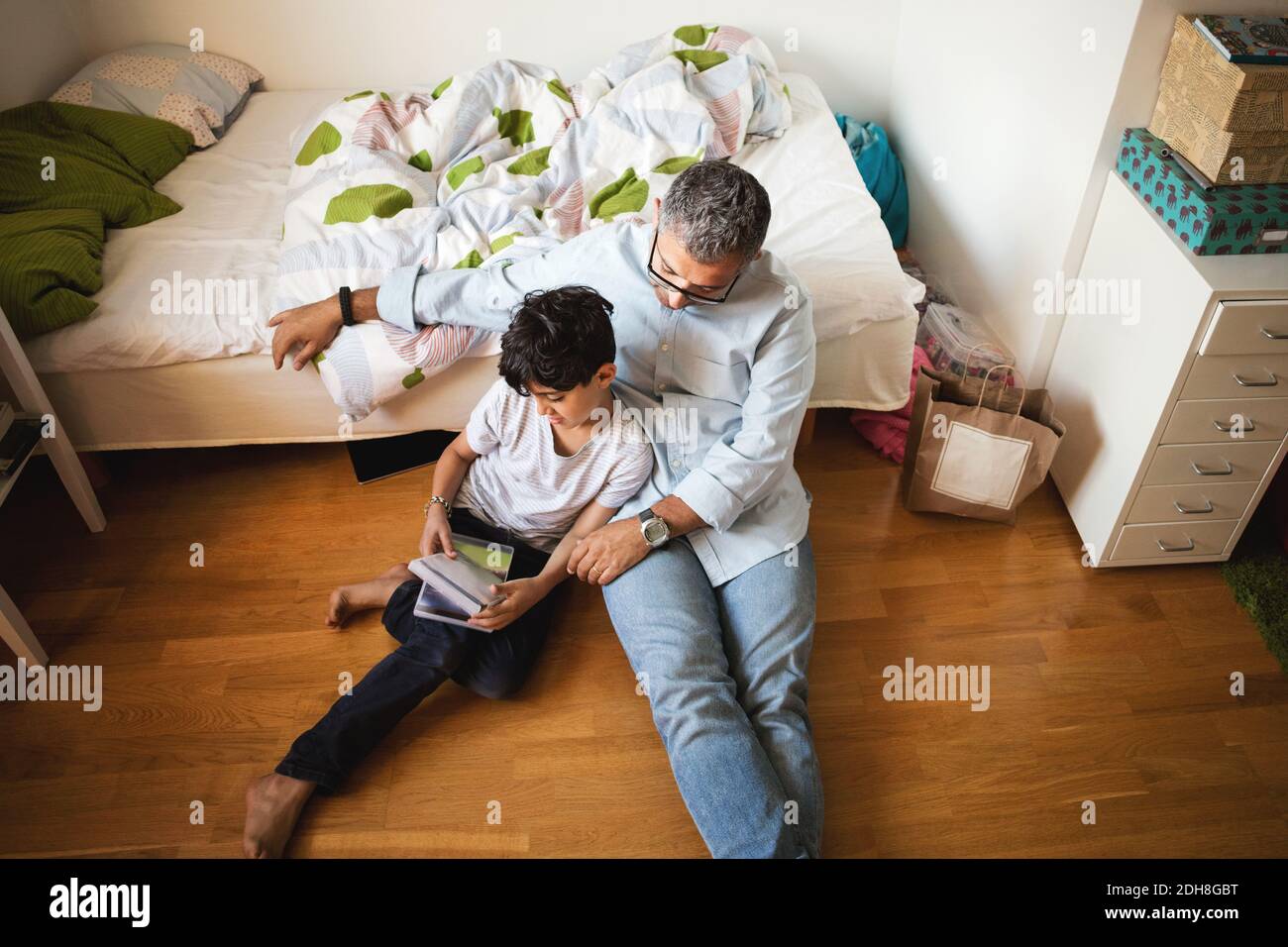 High angle view of father and son reading book while sitting on hardwood floor in bedroom Stock Photo