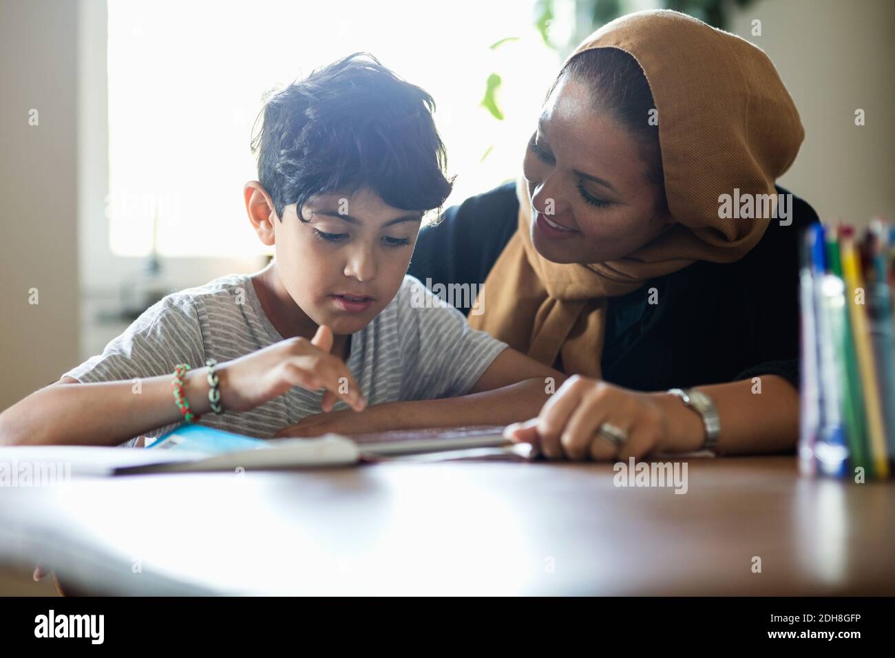 Smiling mother assisting son in using digital tablet while studying at home Stock Photo