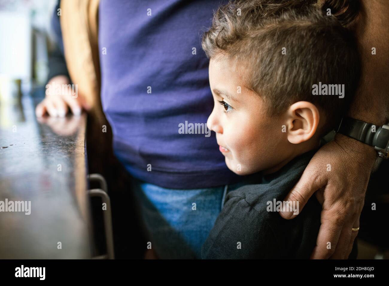 Thoughtful boy looking away while standing by father in kitchen Stock Photo