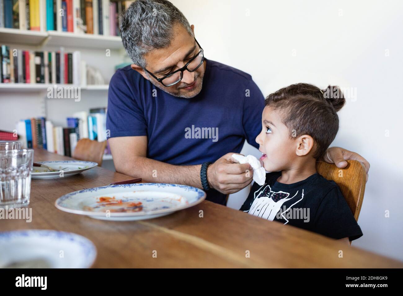 Father wiping son's mouth after lunch at dining table Stock Photo