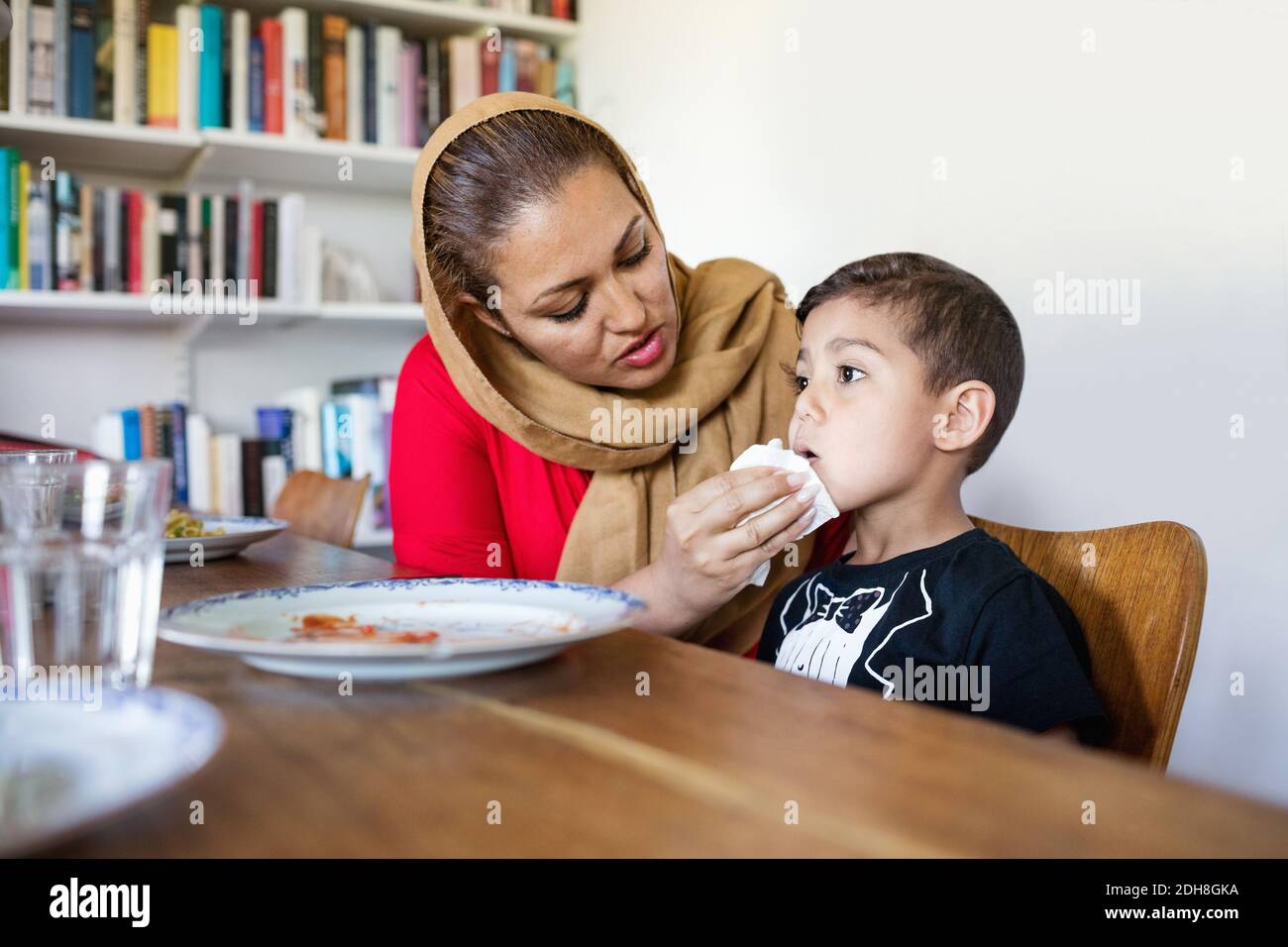 Mother wiping son's mouth after lunch at dining table Stock Photo