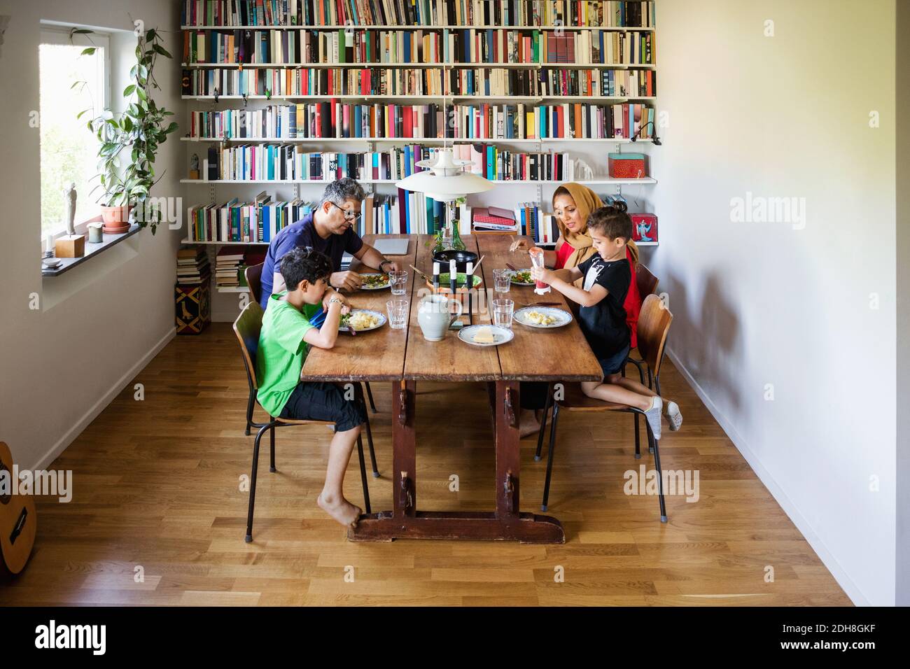 Having Table Family having meal at dining table by bookshelf Stock Photo - Alamy