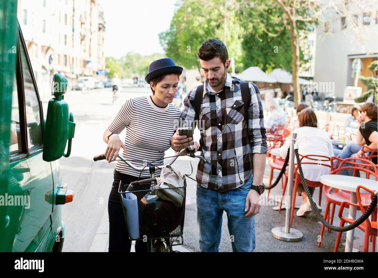 Couple using smart phone while standing by sidewalk cafe Stock Photo