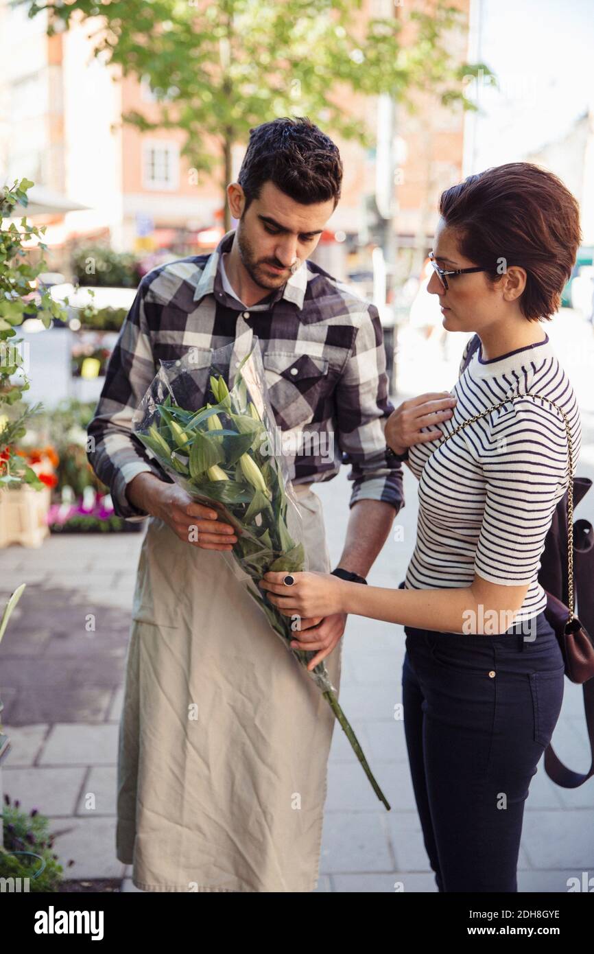 Female customer buying flowers from male owner on sidewalk Stock Photo