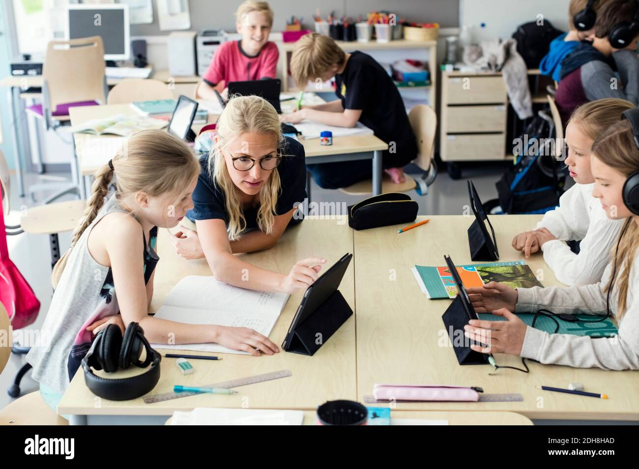 Teacher assisting high school girl using digital tablet in classroom ...