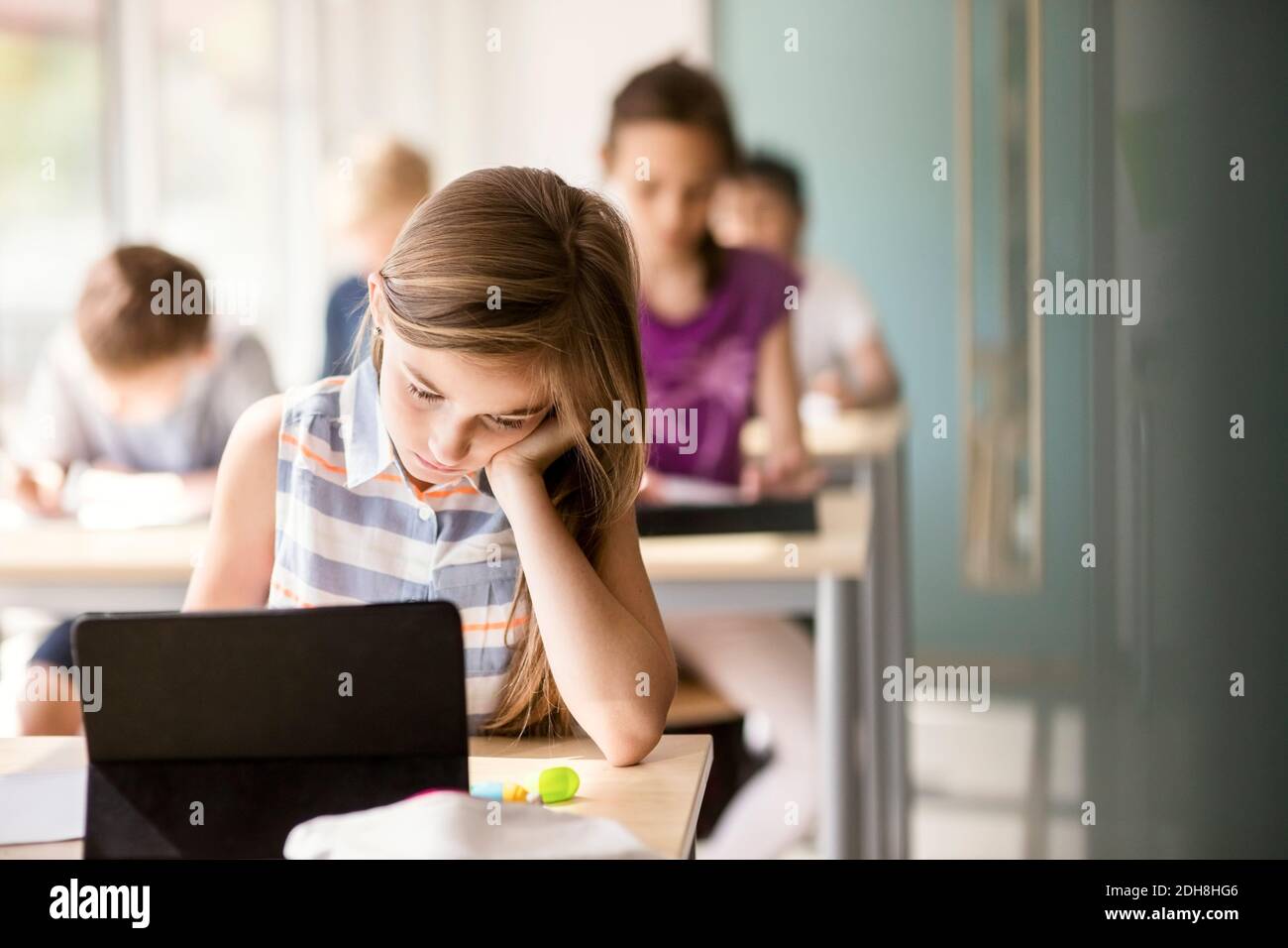 Schoolgirl studying at desk with students in classroom Stock Photo