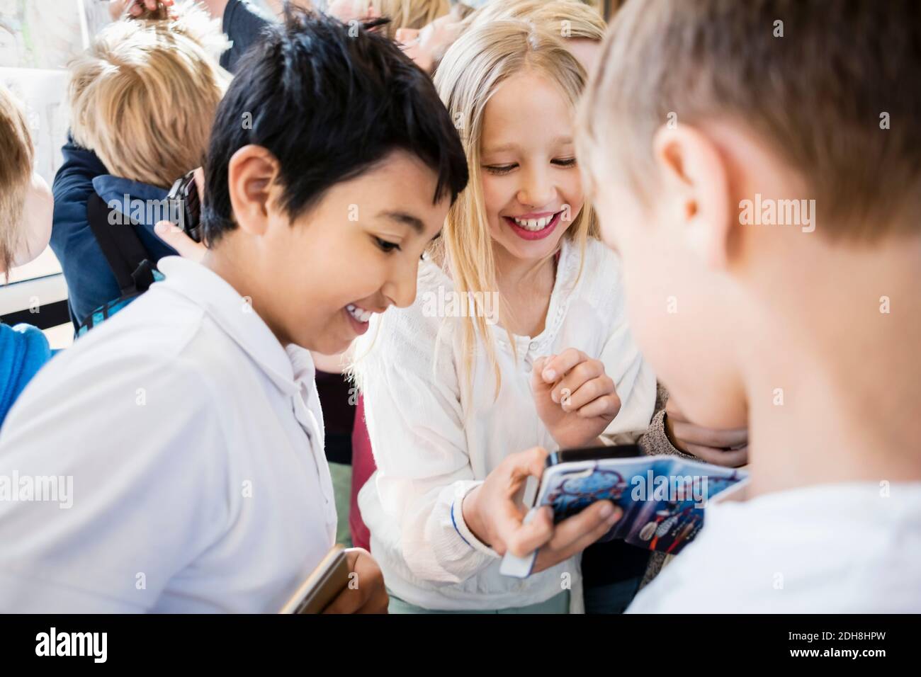 Happy school kids using mobile phone in corridor Stock Photo