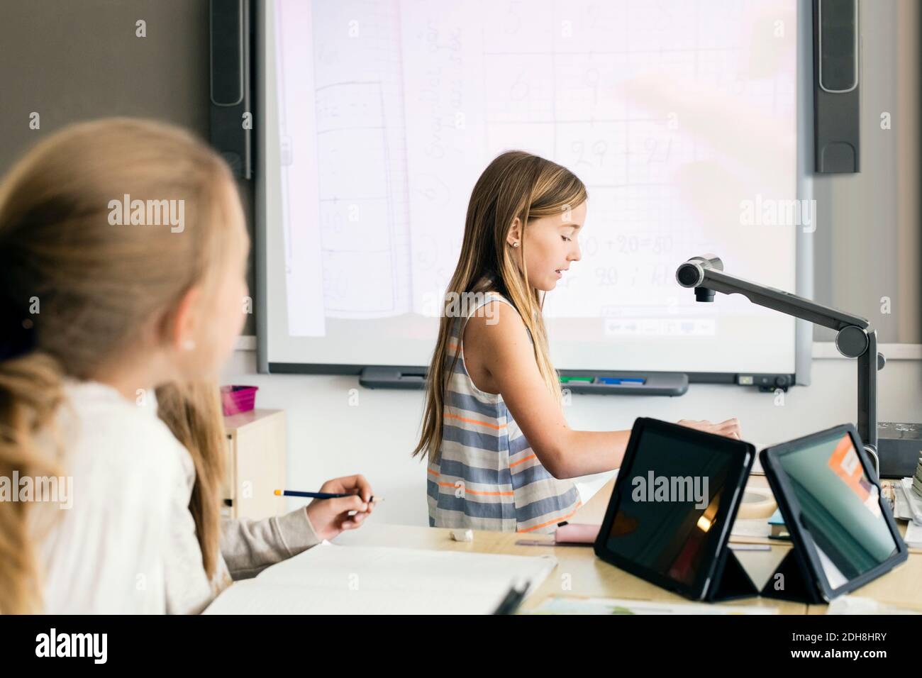 Side view of girl reading document below camera against whiteboard in