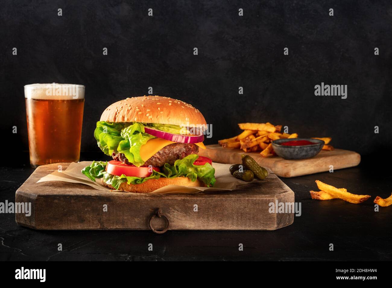 Burger and beer. Hamburger with beef, cheese, onion, tomato, and green salad, with pickles and French fries, a side view on a bl Stock Photo