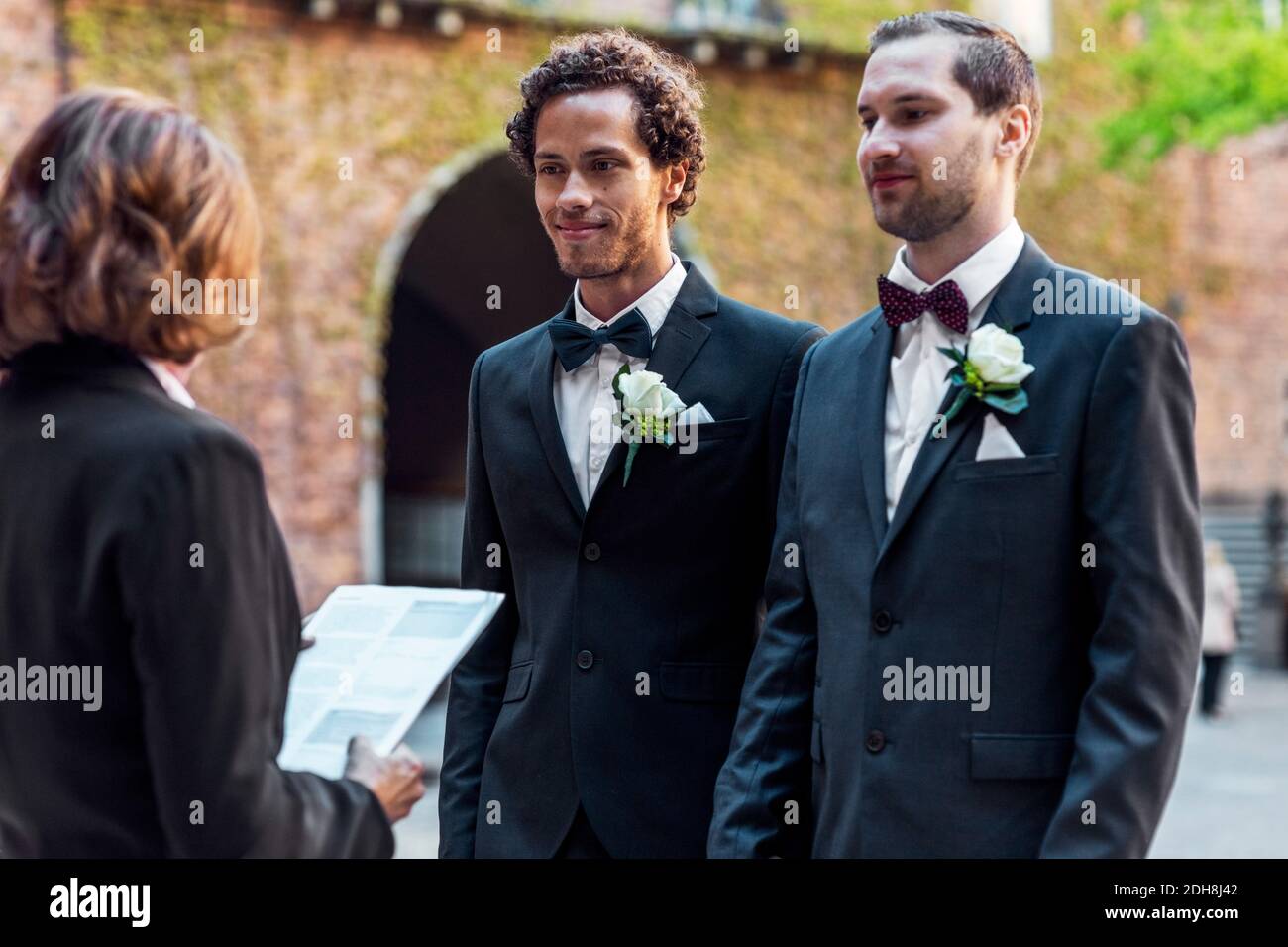 Gay couple standing in front of senior priest during wedding ceremony Stock Photo