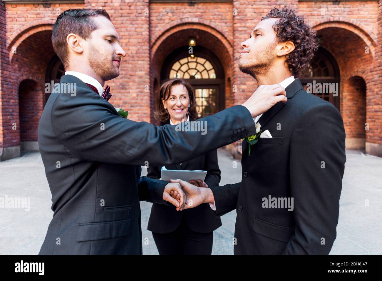 Man adjusting bow tie of gay partner in front of priest during wedding ceremony Stock Photo