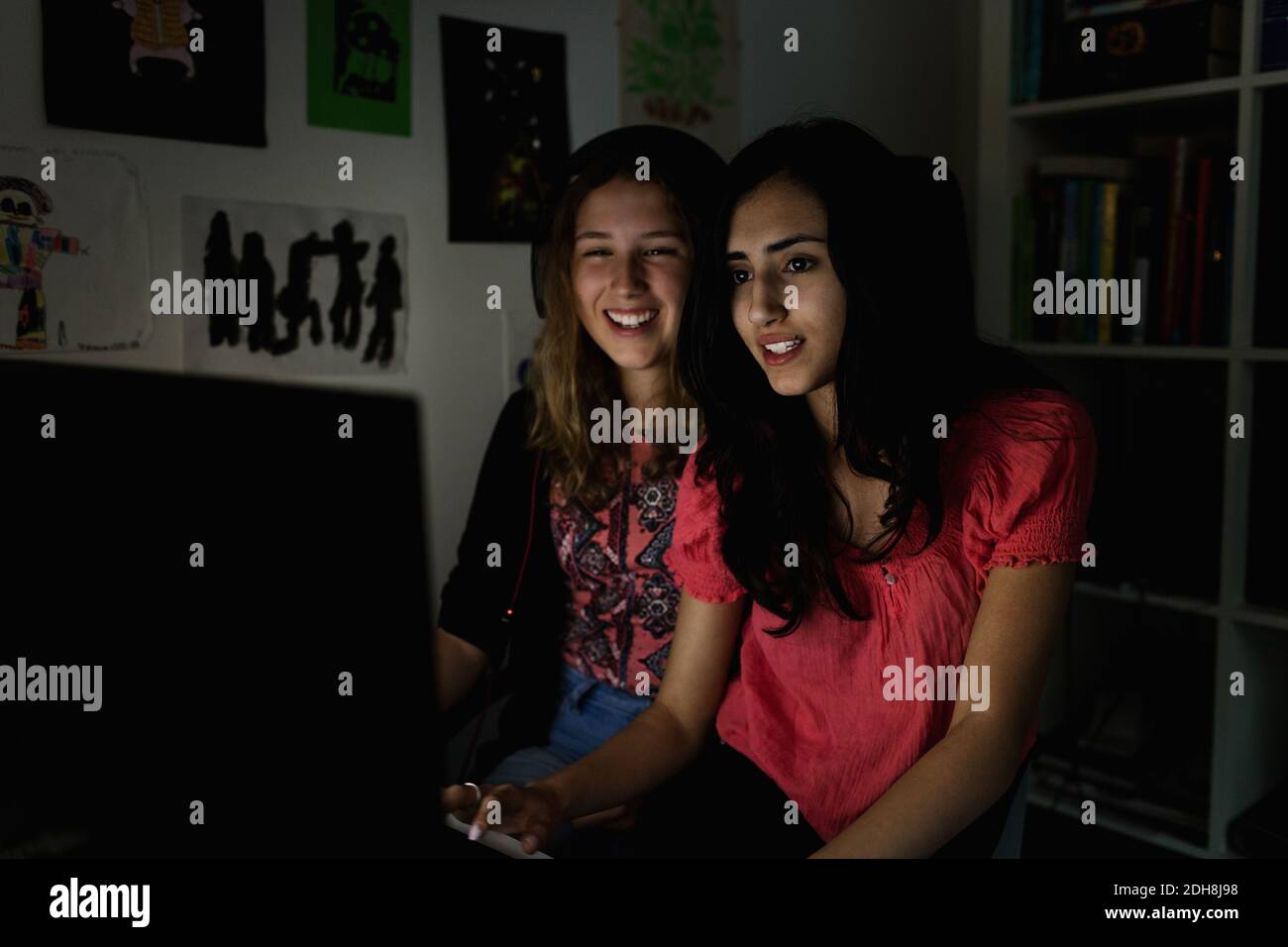 Happy teenage girls using computer in darkroom at home Stock Photo