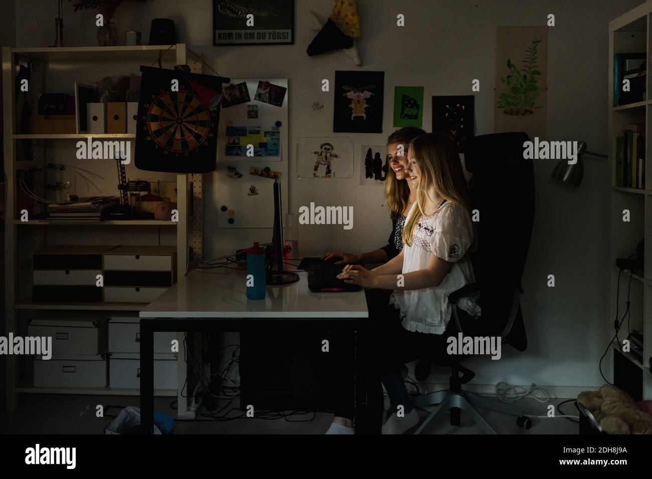 Teenage girls using computer at table in darkroom at home Stock Photo
