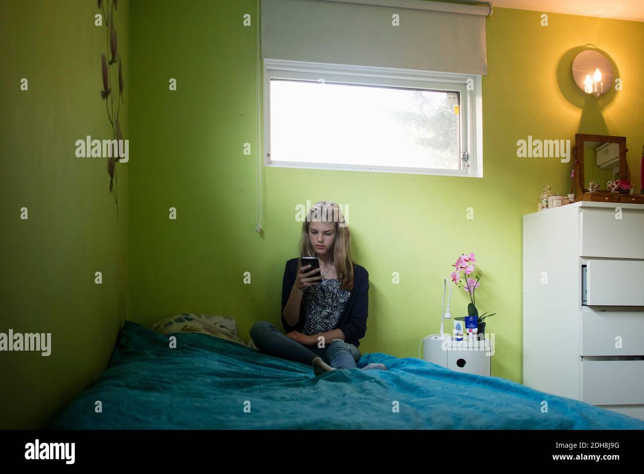 Teenage girl using smart phone while sitting on bed at home Stock Photo ...